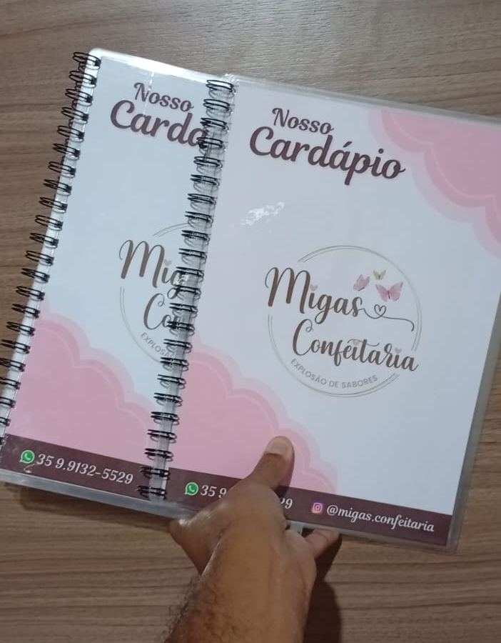 Dois cardápios da Migas Confeitaria encadernados em espiral, com capa rosa e branca, logotipo e contatos no rodapé